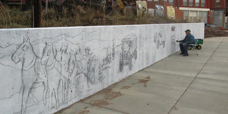 Artist starting drawing of mural on retaining wall along sidewalk on North 4th Street.